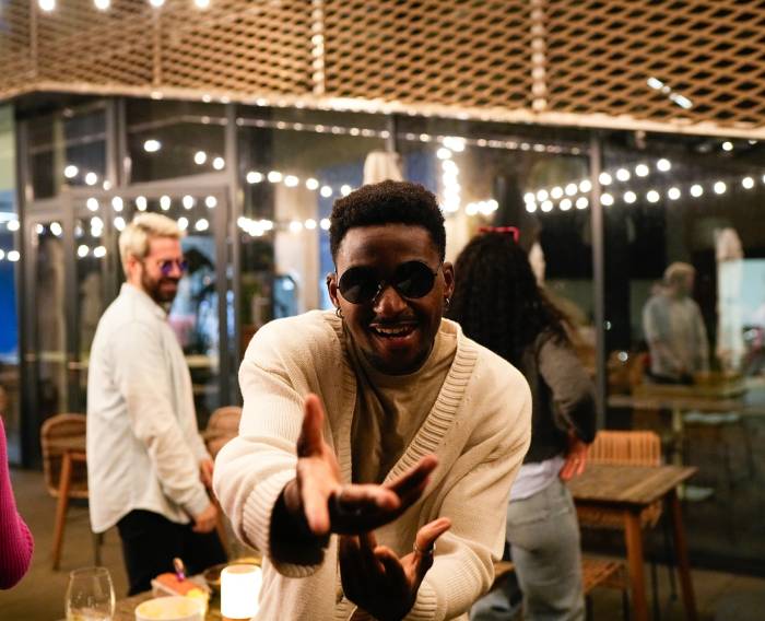 Happy young man dancing and enjoying an evening party with friends outdoors under string lights